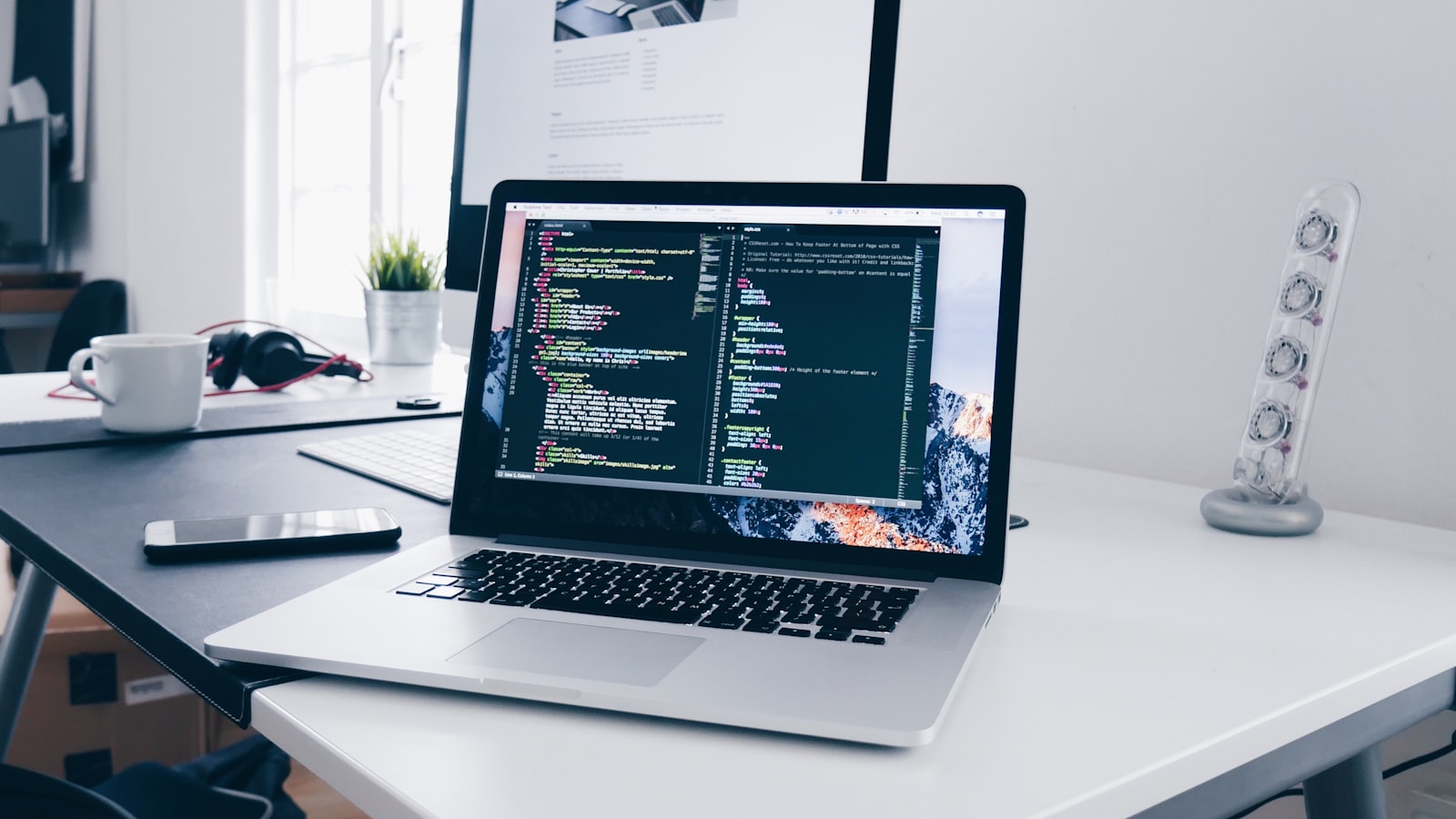 A laptop on a tidy desk showing code and a task list, lit by soft daylight