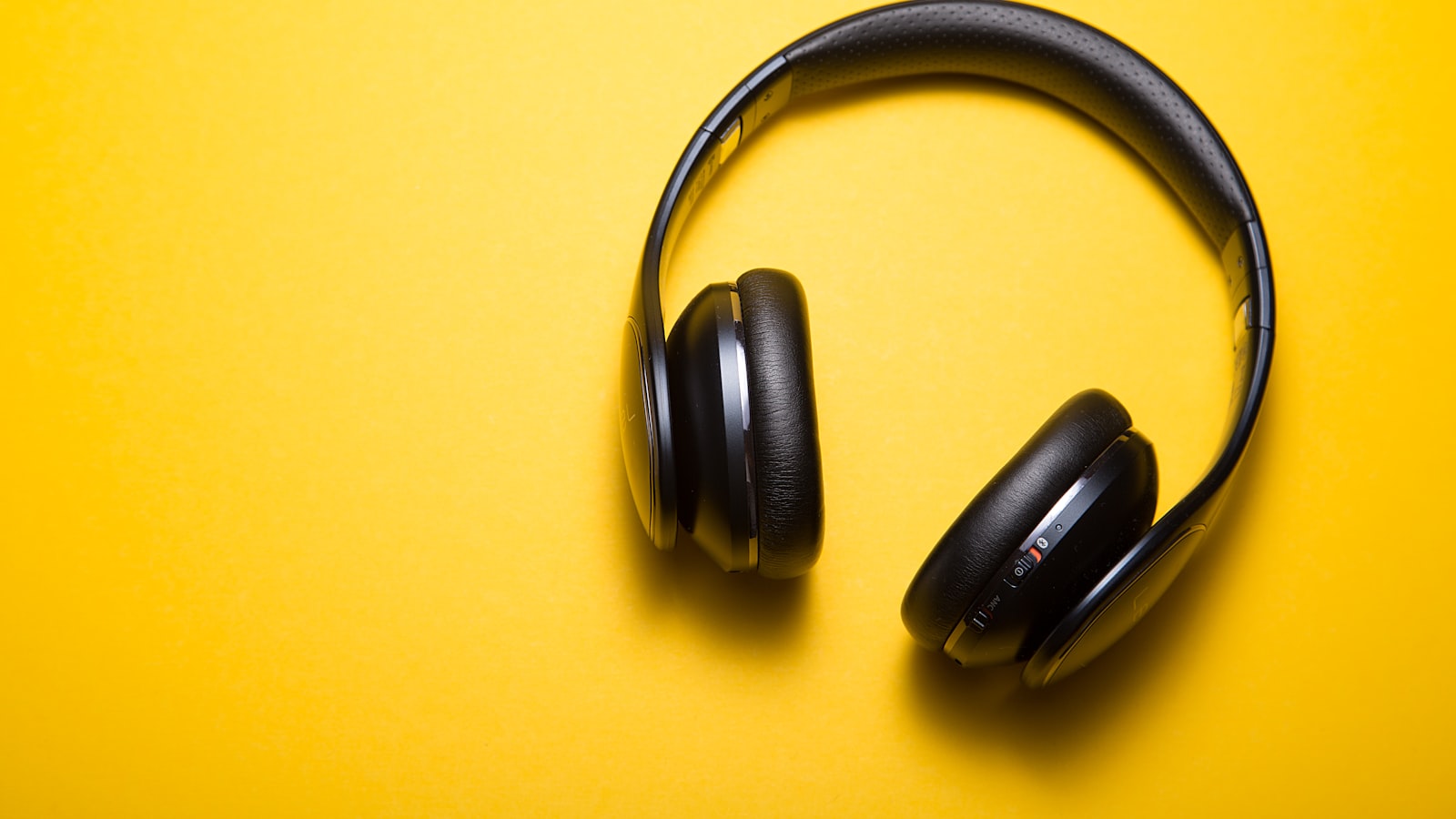A pair of wireless headphones resting next to a phone showing a settings screen